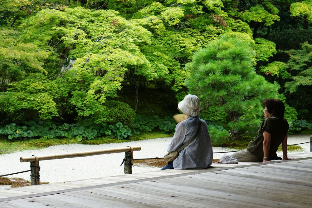 Two people sitting quietly on a temple veranda overlooking a garden